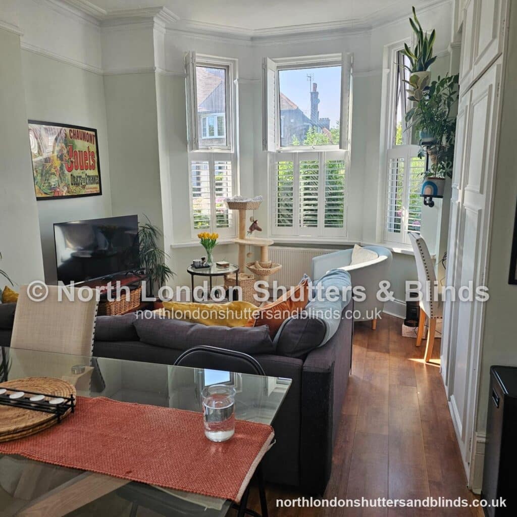 White tier-on-tier plantation shutters on a bay window in a living room, with the shutters open by shutter fitters in Barnet, North London