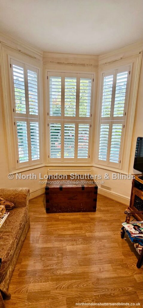 White tier-on-tier plantation shutters on a bay window in a living room by shutter fitters in Barnet, North London