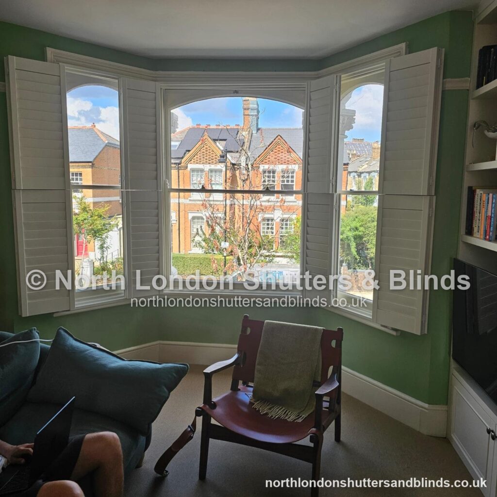 White tier-on-tier plantation shutters on a bay window in a living room, with the shutters folded open by shutter fitters in Barnet, North London