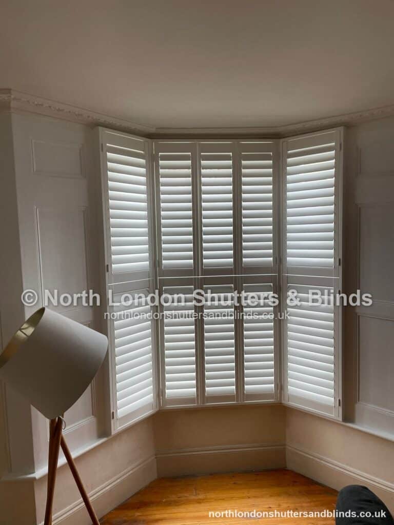 White tier-on-tier plantation shutters on a bay window in a living room by shutter fitters in Barnet, North London