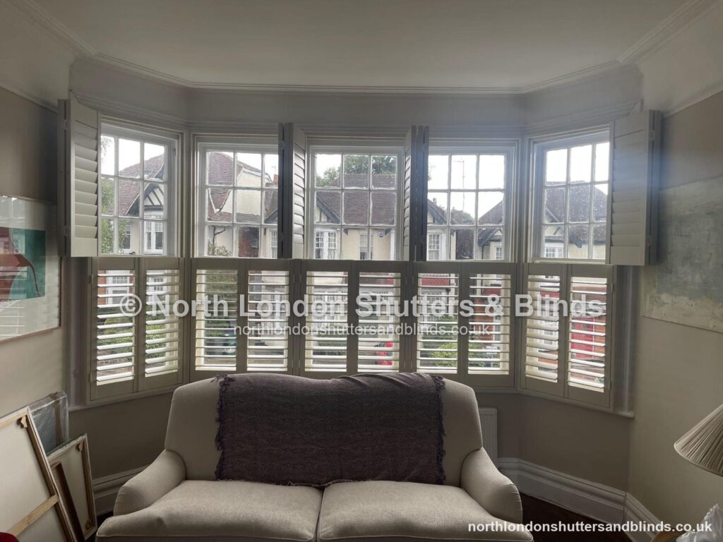 White tier-on-tier plantation shutters on a large bay window in a living room by shutter fitters in Barnet, North London