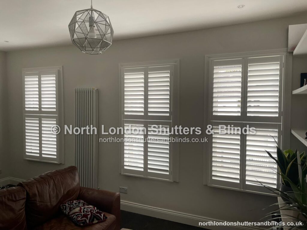 White tier-on-tier plantation shutters on three windows in a living room by shutter fitters in Barnet, North London