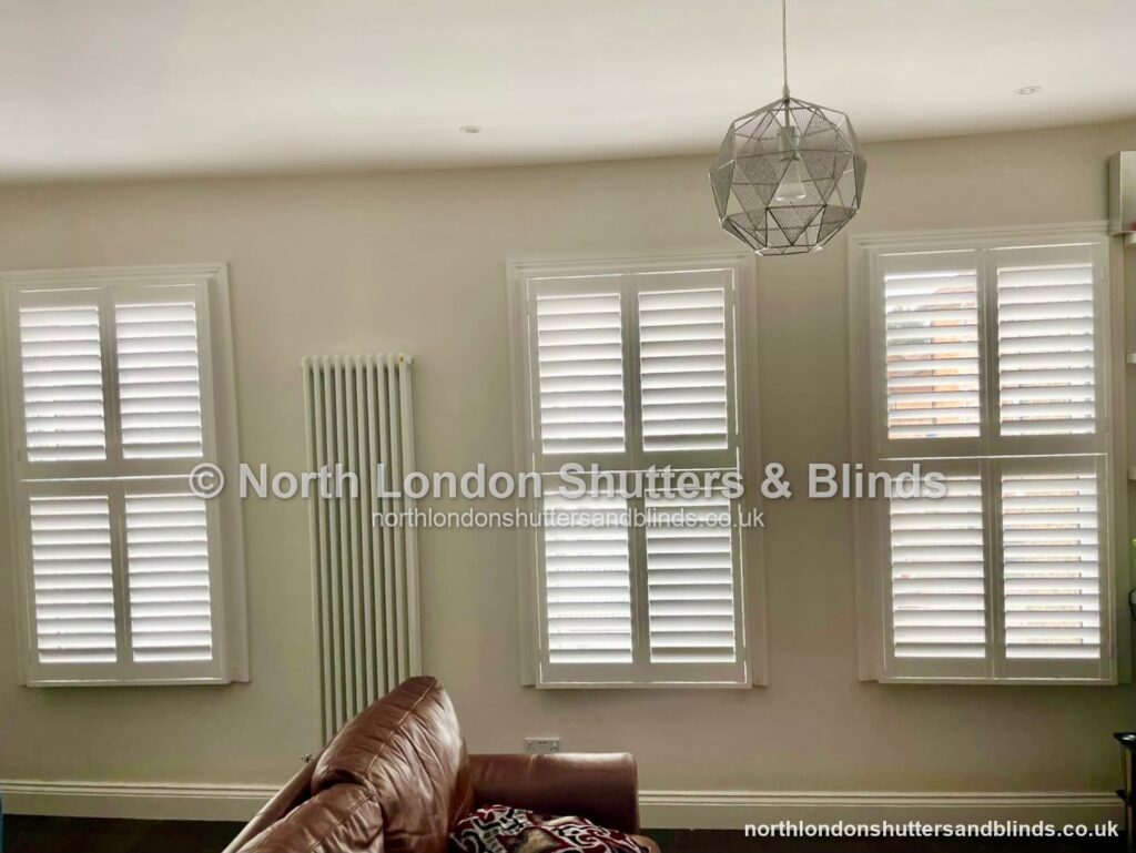 White tier-on-tier plantation shutters on two windows in a living room by shutter fitters in Barnet, North London