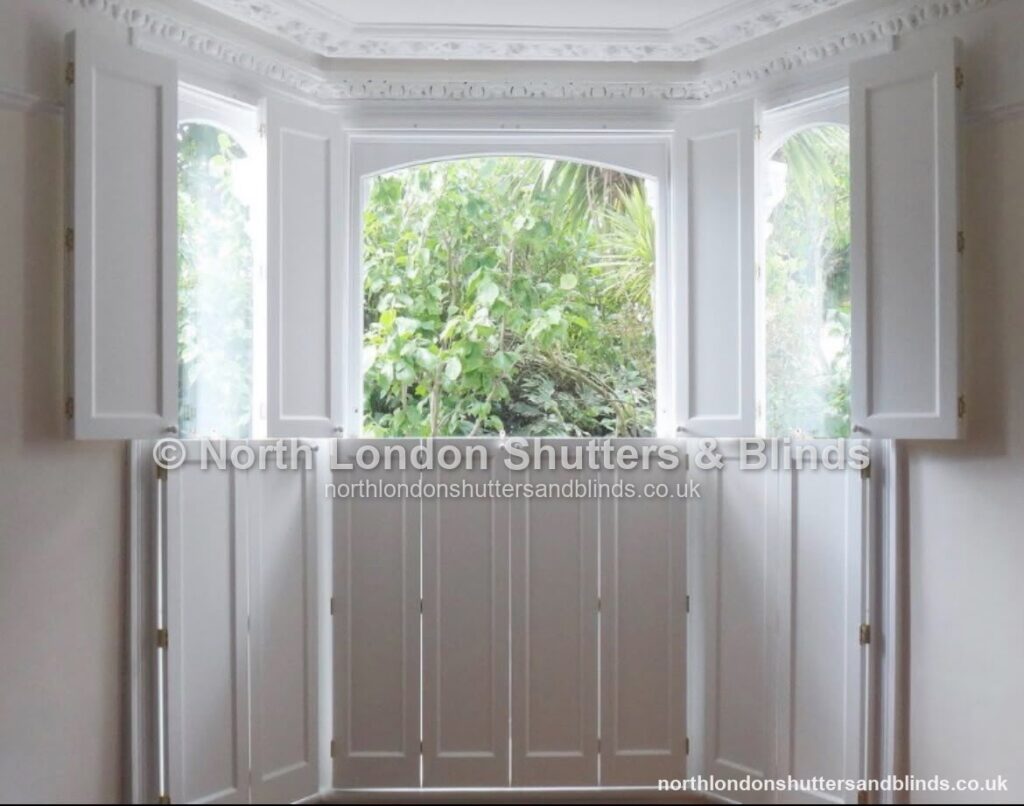 White solid panel shutters on a bay window, with the top panels folded open by shutter fitters in Barnet, North London