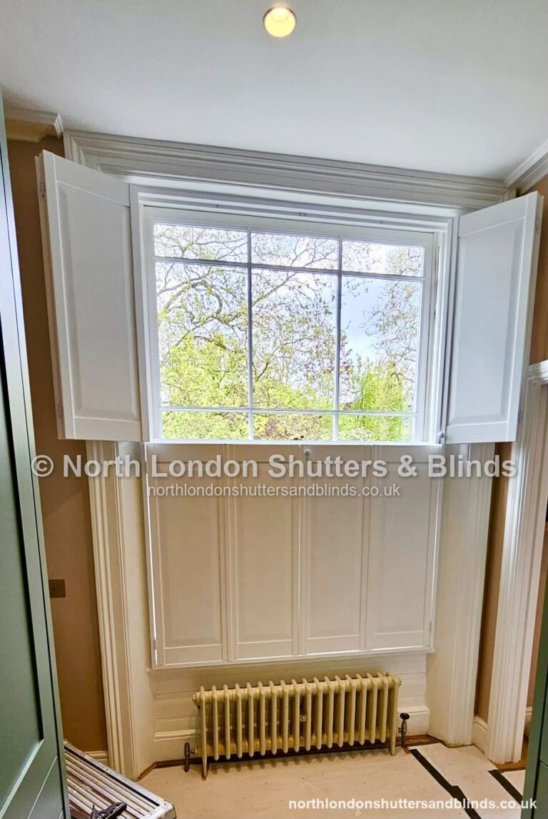 White solid panel shutters on a sash window, with the panels folded open by shutter fitters in Barnet, North London