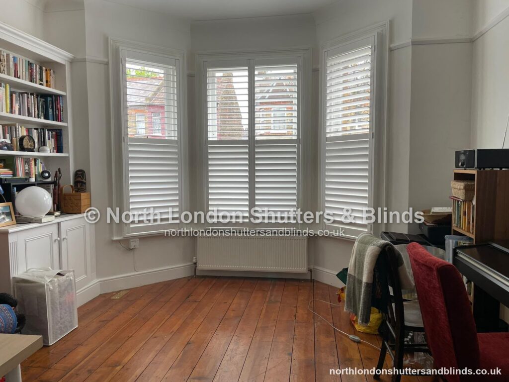 White tier-on-tier plantation shutters on a bay window in a study by shutter fitters in Barnet, North London